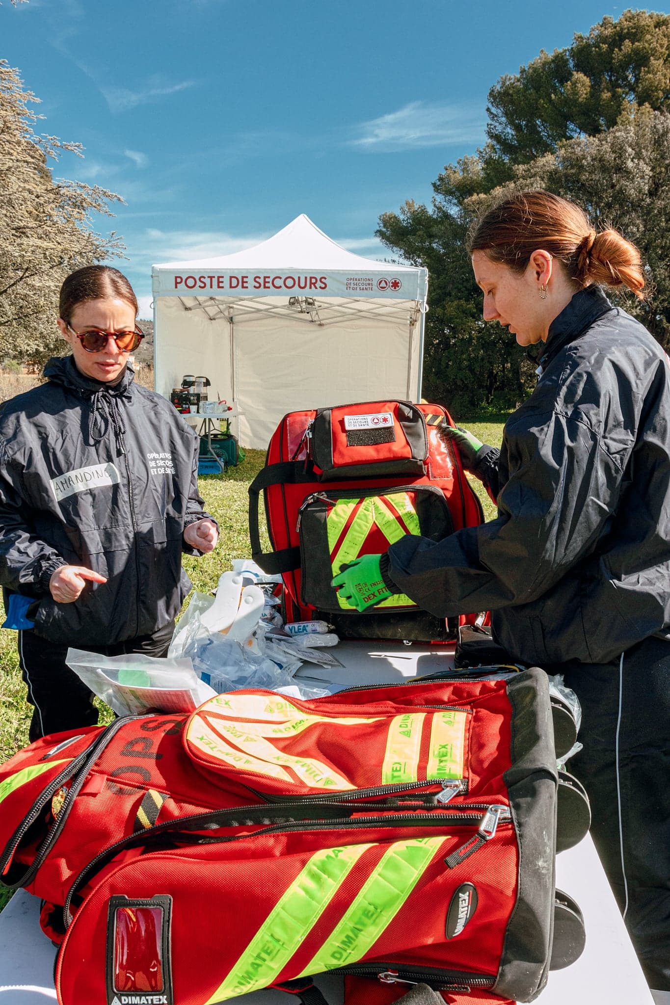 Deux secouristes OPSAN inspectant les sacs d'intervention devant la tente Poste de Secours