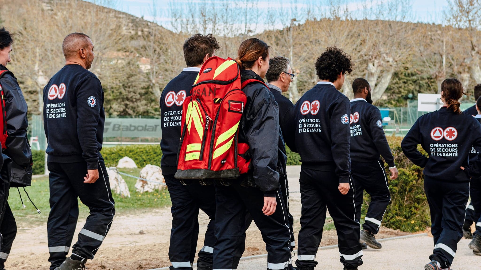 Équipe OPSAN en tenue d'intervention, l'un porte un sac rouge de premiers secours, marchant ensemble